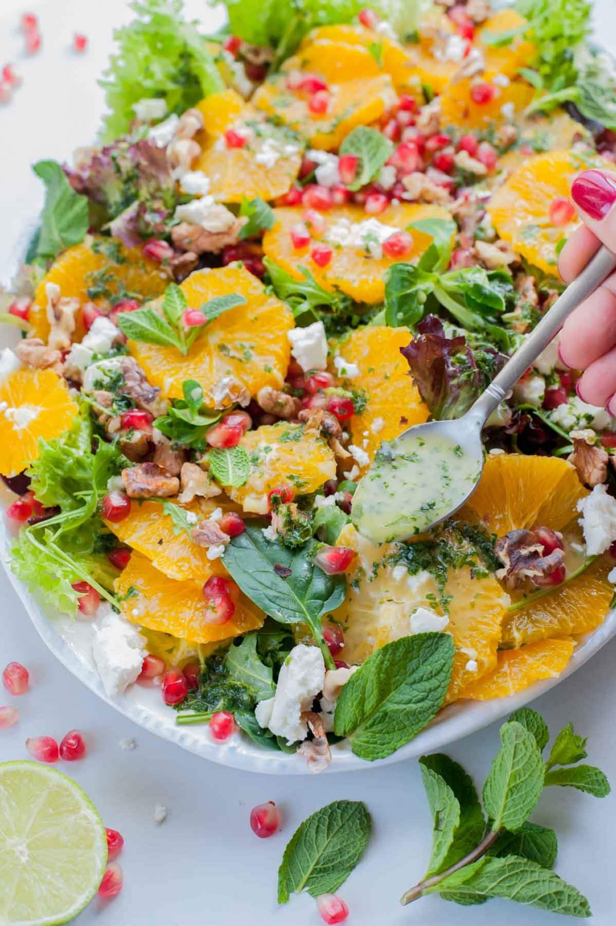 mint lime vinaigrette is being spooned over the orange pomegranate salad