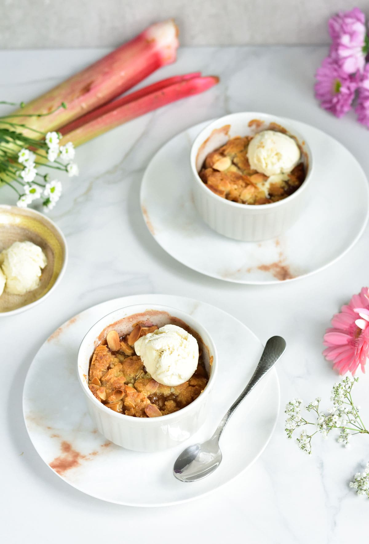 2 ramekins with rhubarb crumble, flowers scattered around