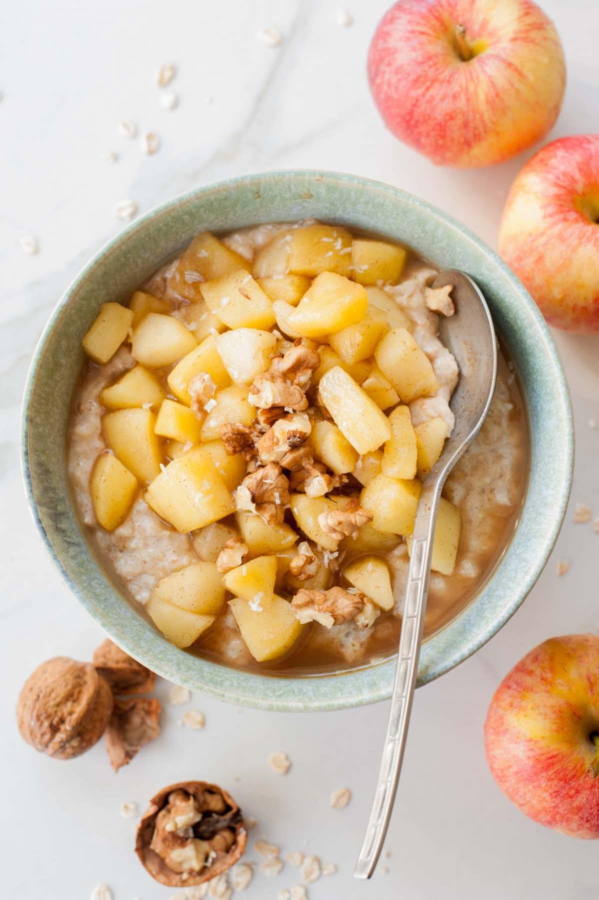 apple cinnamon oatmeal in a green bowl, walnuts and apples scattered around