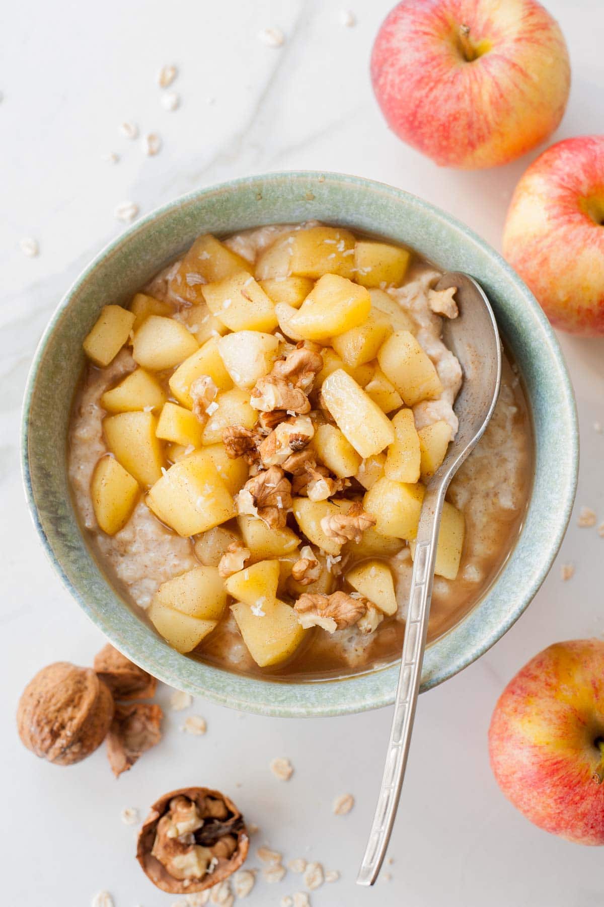 Cinnamon oatmeal topped with apple cinnamon apples and walnuts in a green bowl.