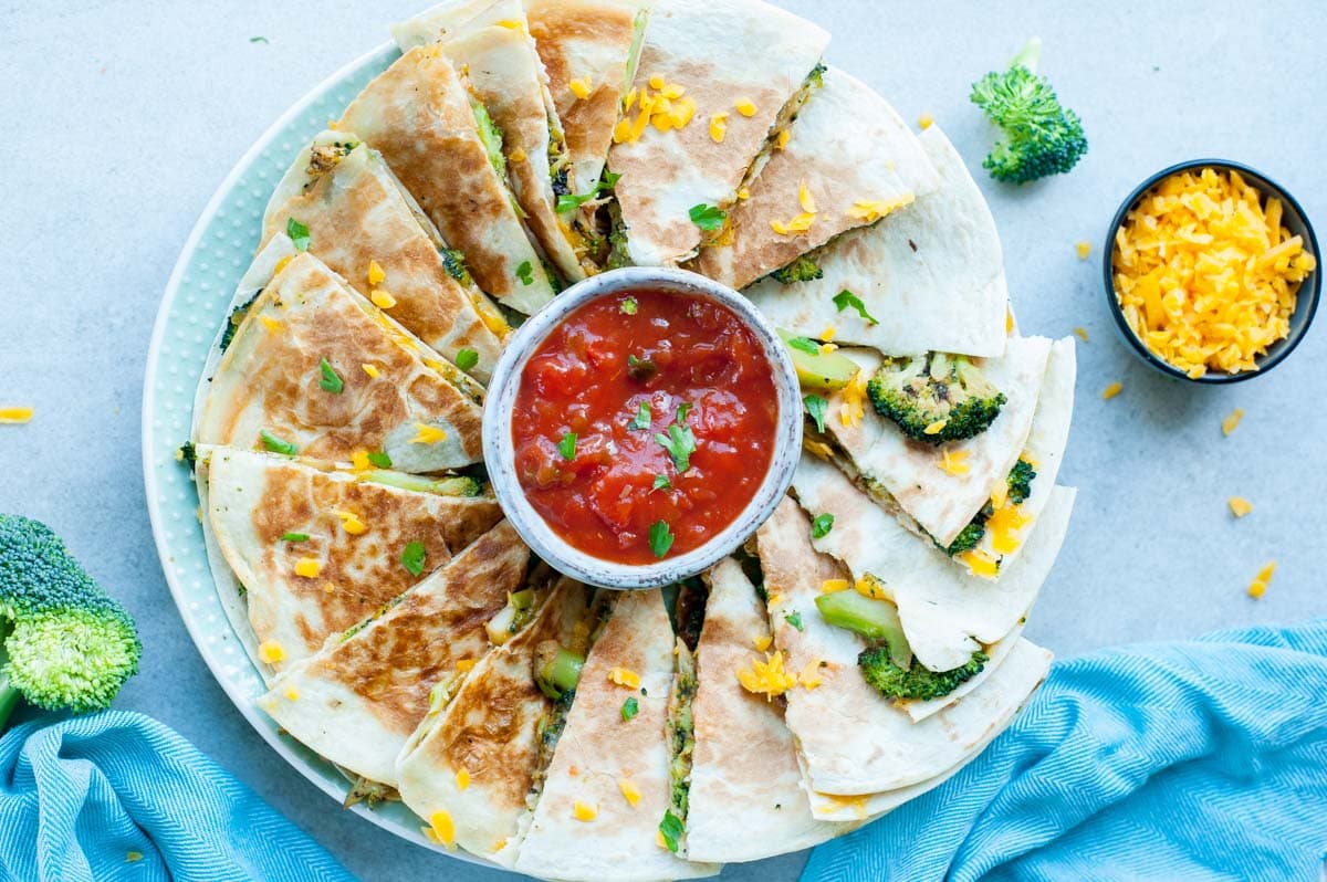 Broccoli quesadillas with cheddar on a plate with tomato salsa in the middle.