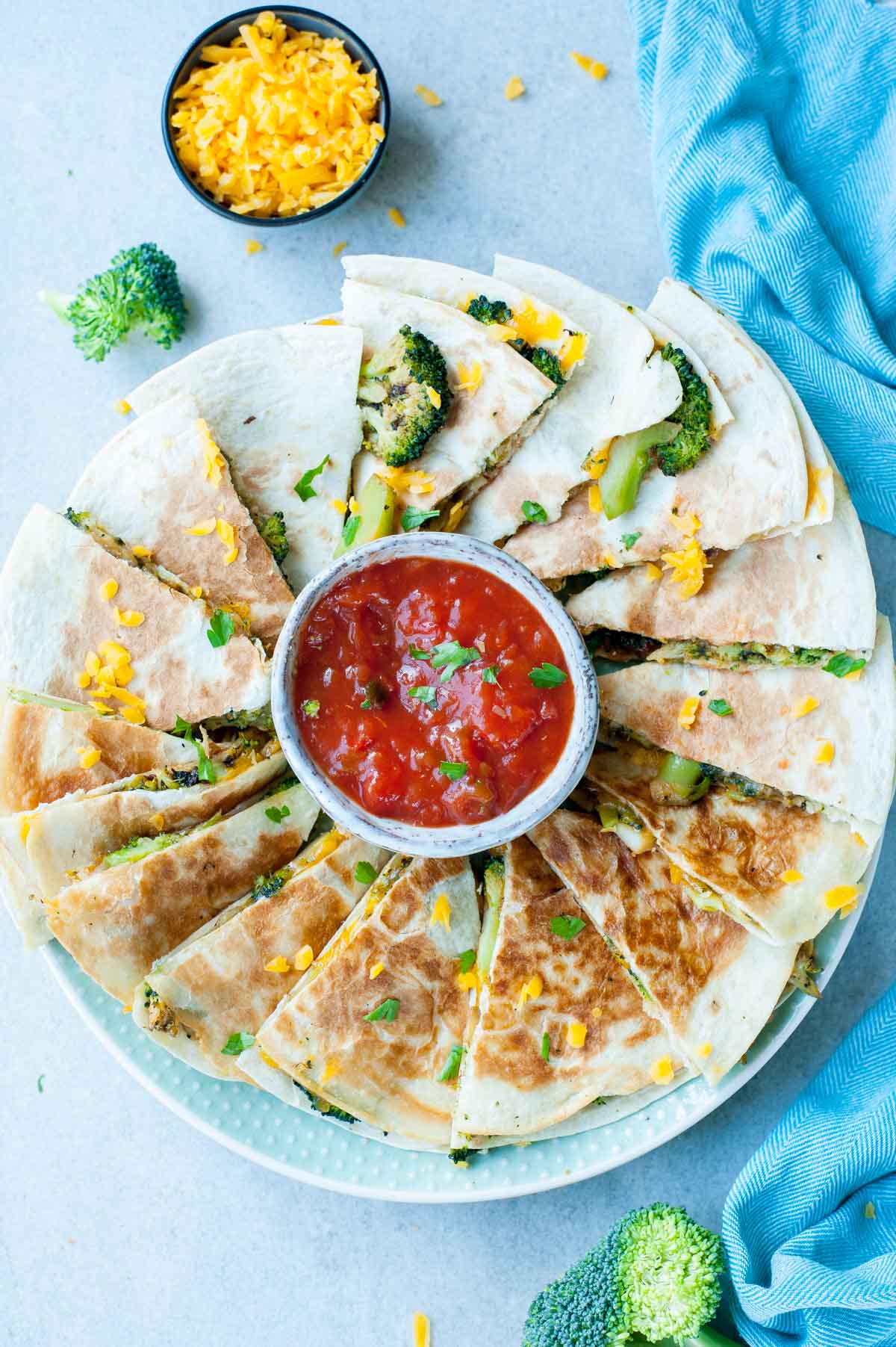 Broccoli quesadilla on a green plate with a small bowl with tomato salsa.