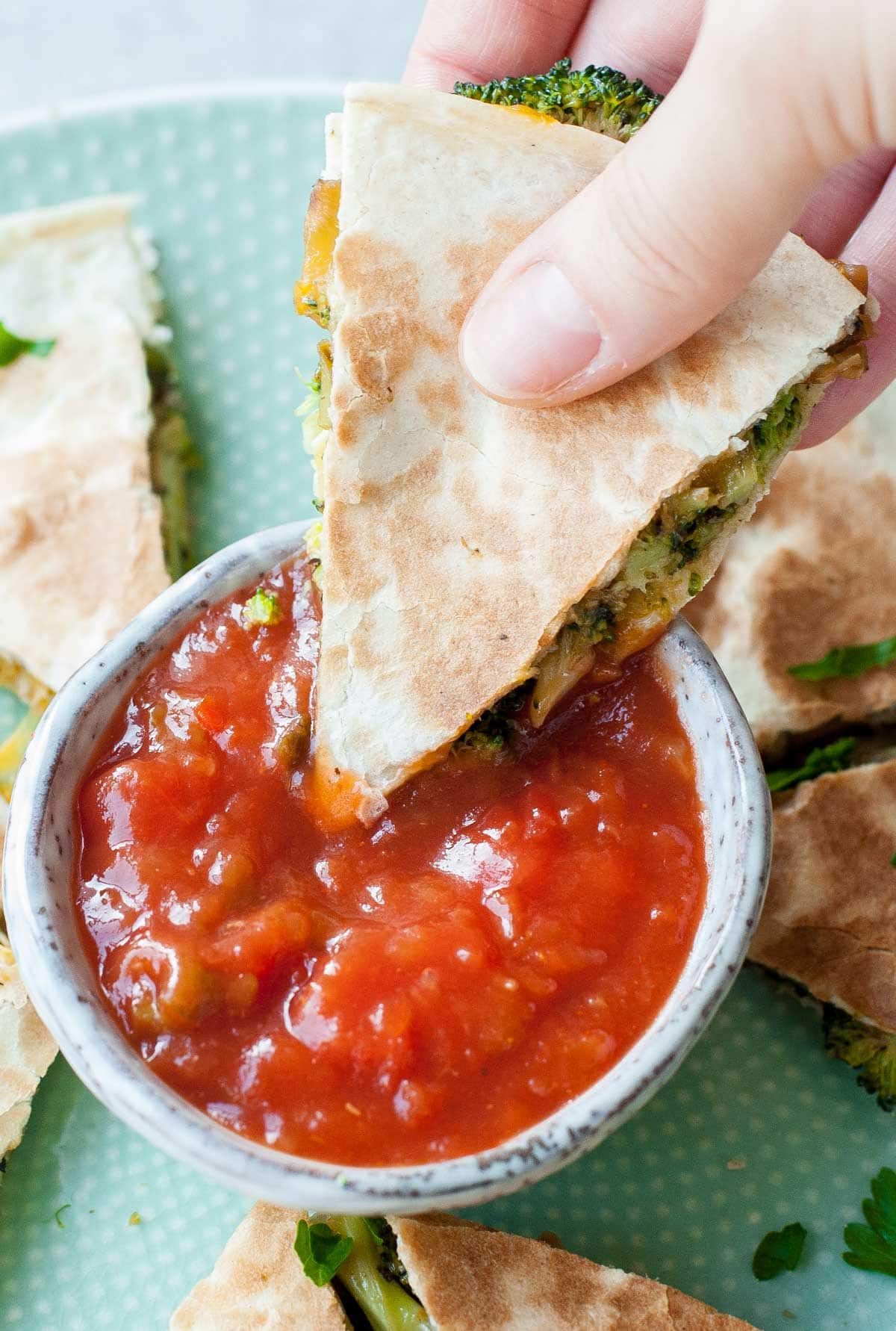 Broccoli quesadillas are being dipped in tomato salsa.