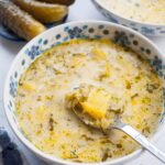 dill pickle soup in a white-blue bowl, fermented cucumbers in the background