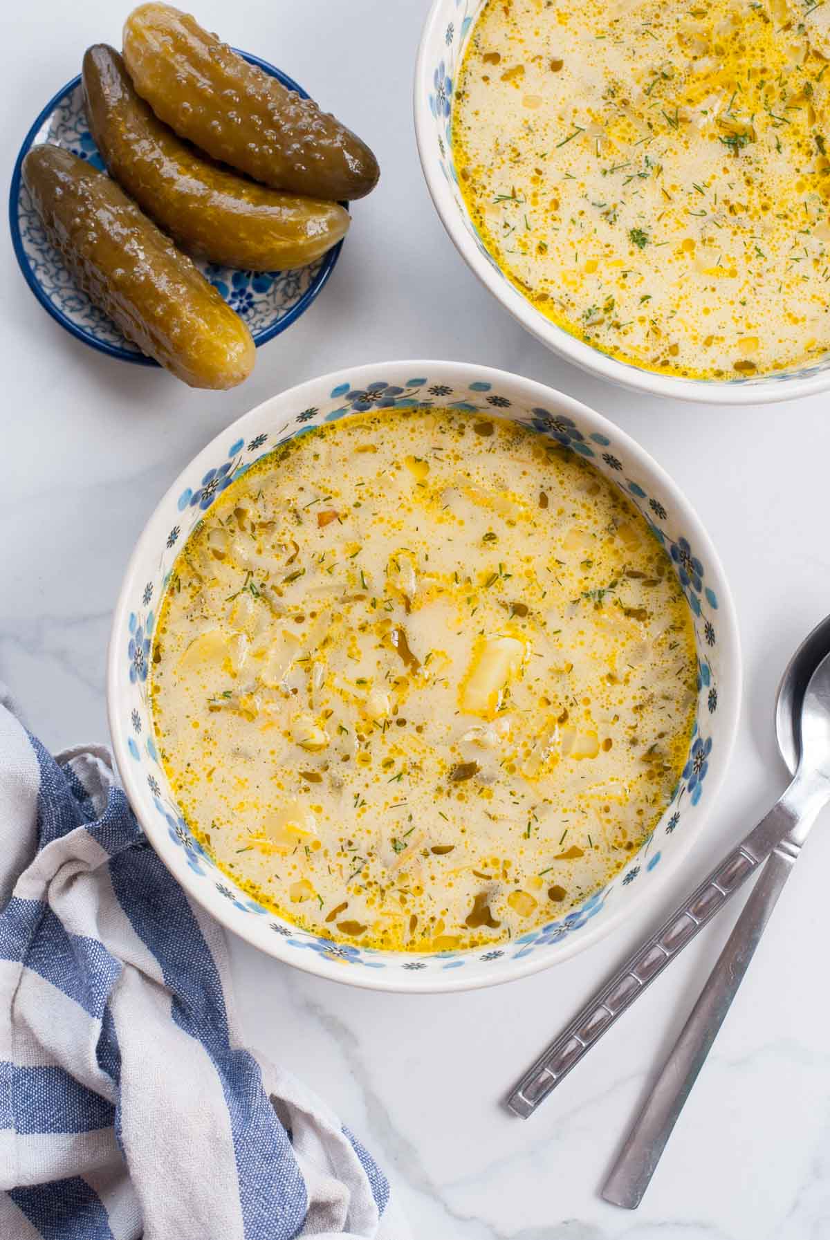 Two bowls with dill pickle soup. Cucumbers in brine on a small plate on the side.