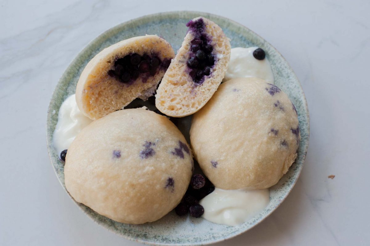 Steamed buns stuffed with blueberries on a green plate.