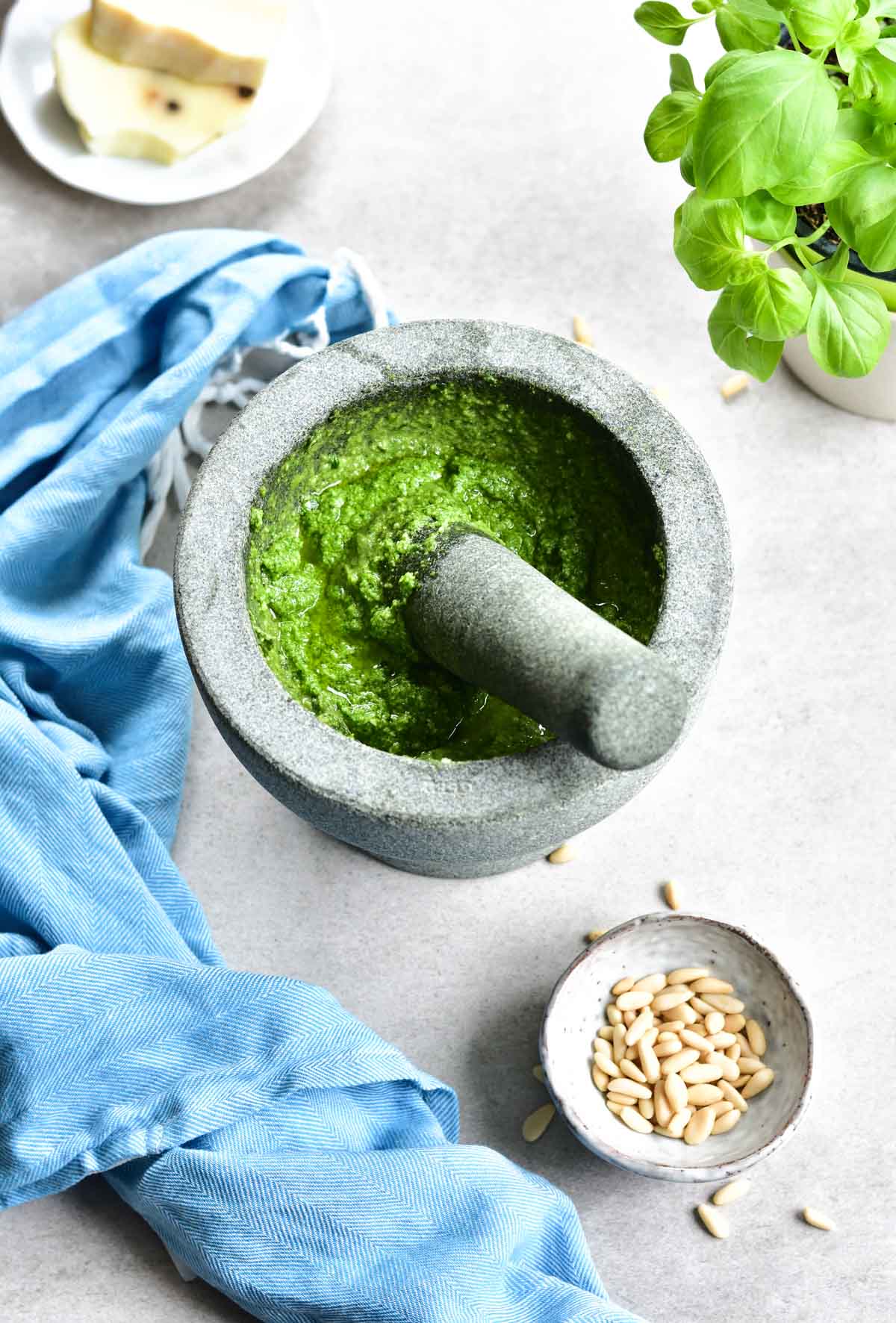 Basil pesto in a granite mortar. Kitchen cloth and pine nuts in the background.