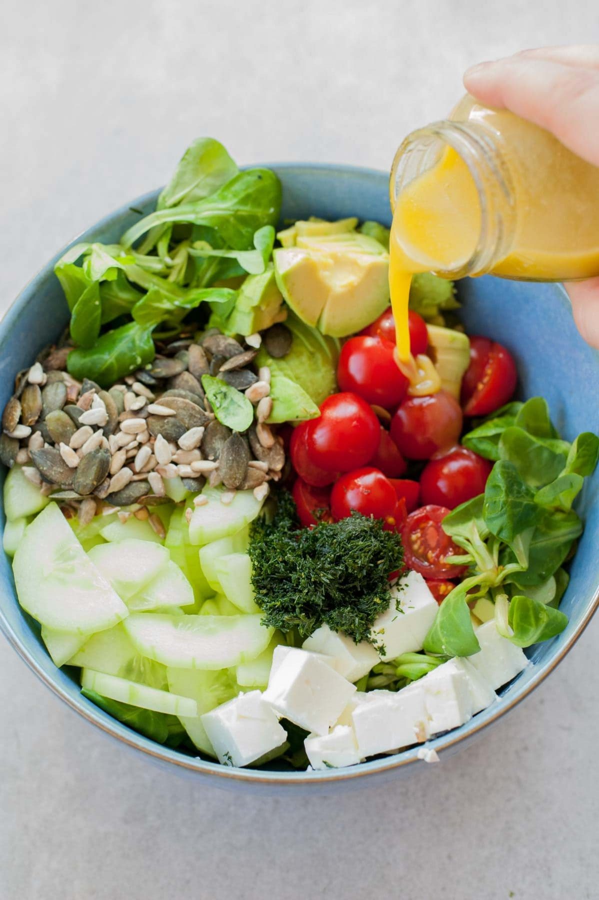 honey mustard vinaigrette is being poured over cucumber avocado tomato salad