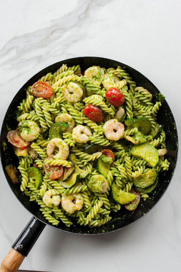 Ready shrimp pesto pasta with zucchini in a black frying pan.