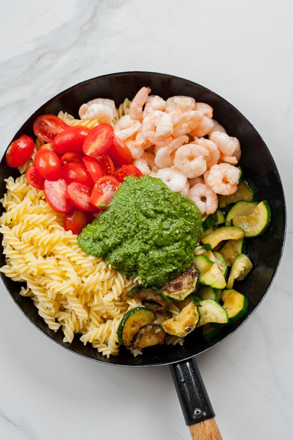 All the ingredients for the shrimp pesto pasta in a black frying pan.