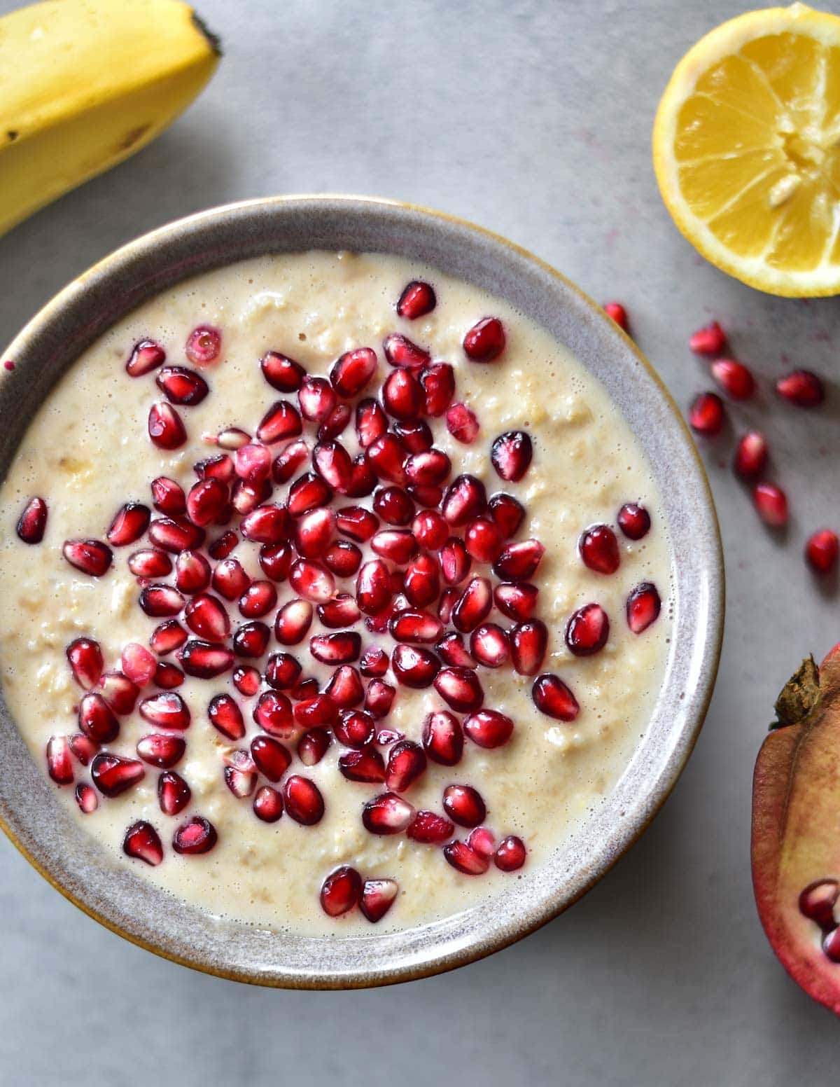 A close up picture of banana peanut butter oatmeal sprinkled with pomegranate seeds on top, in a grey bowl.