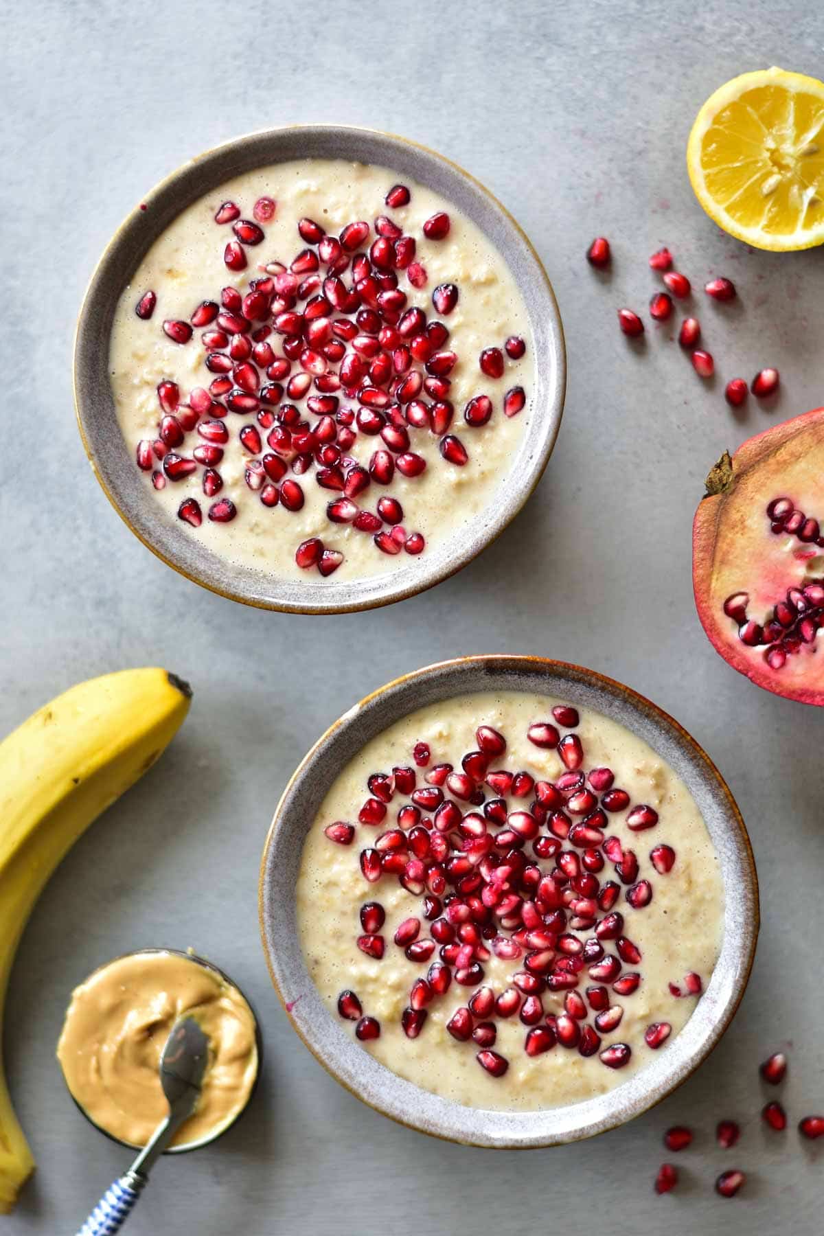 2 bowl with banana peanut butter oatmeal with pomegranate seeds on top