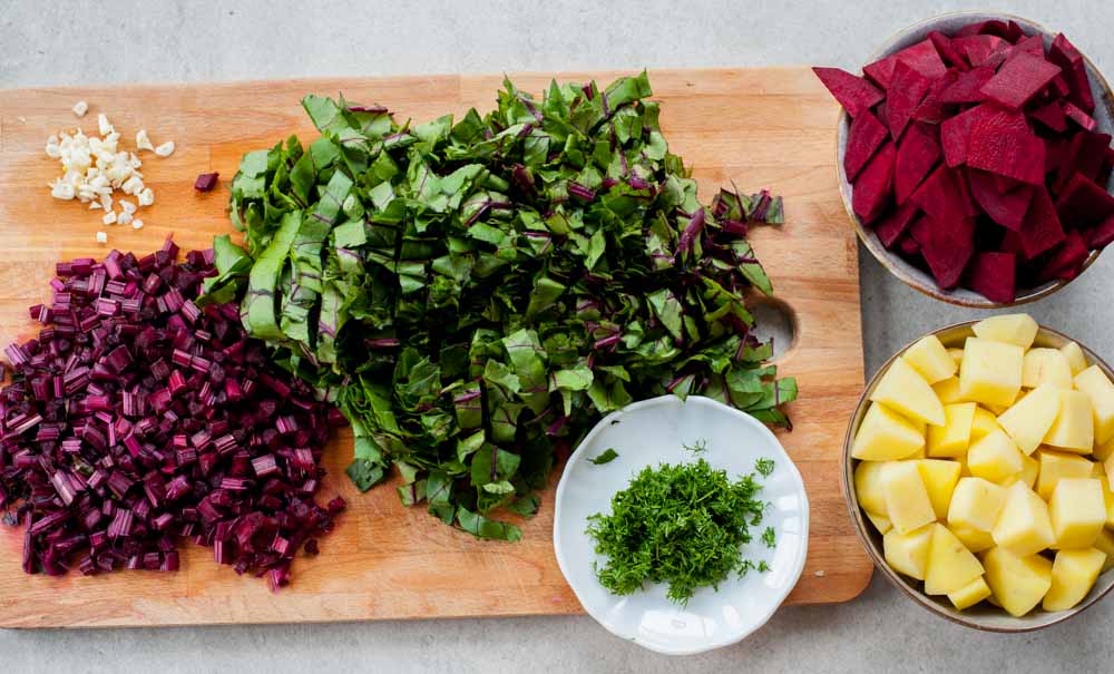 chopped beets, their stems and leaves, potatoes, dill and garlic on a chopping board