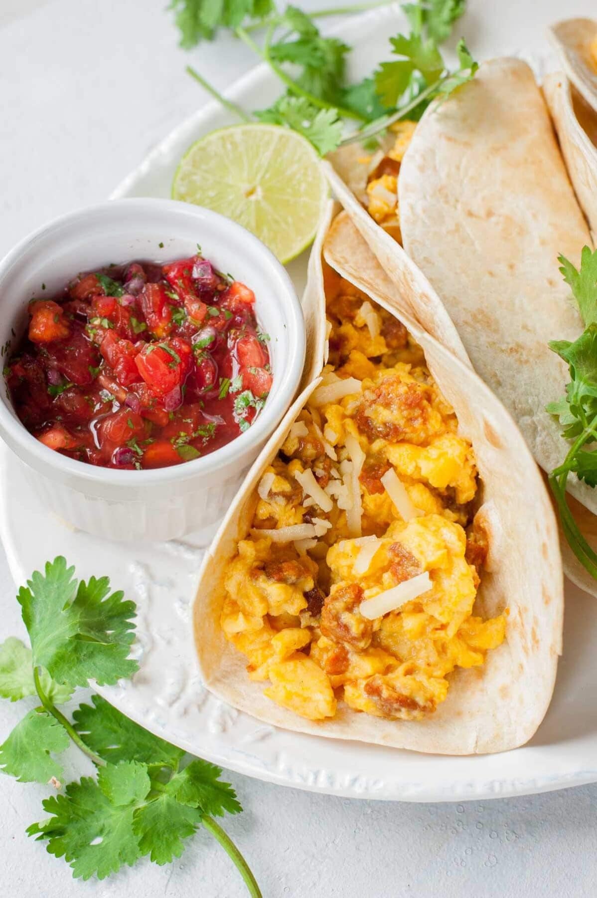 Tacos with scrambled eggs and chorizo, small bowl with pico de gallo on the side.