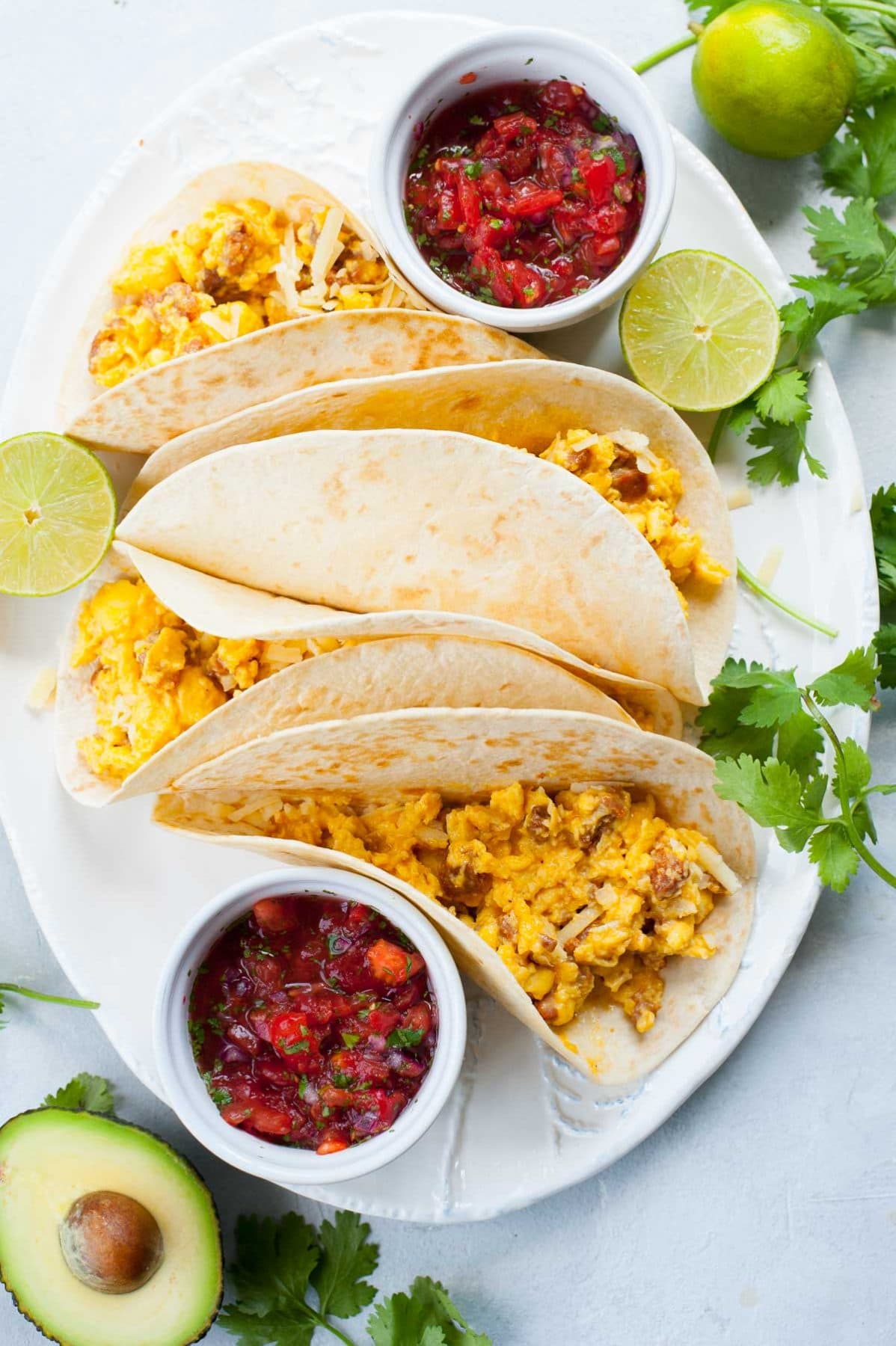 Big white plate with 4 breakfast tacos and two small bowl with pico de gallo.