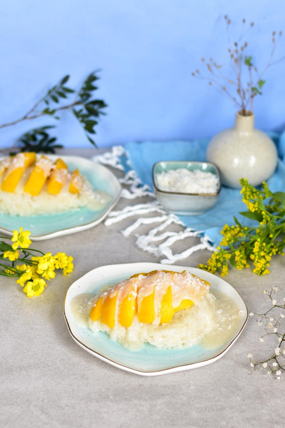 two plates with coconut sticky rice with mango and coconut sauce surrounded with flowers