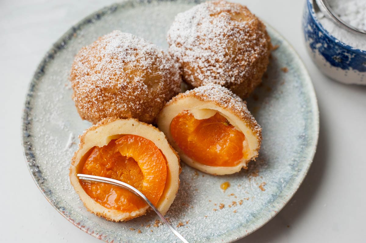 A fork cutting into a apricot dumpling with breadcrumb cinnamon sugar topping.