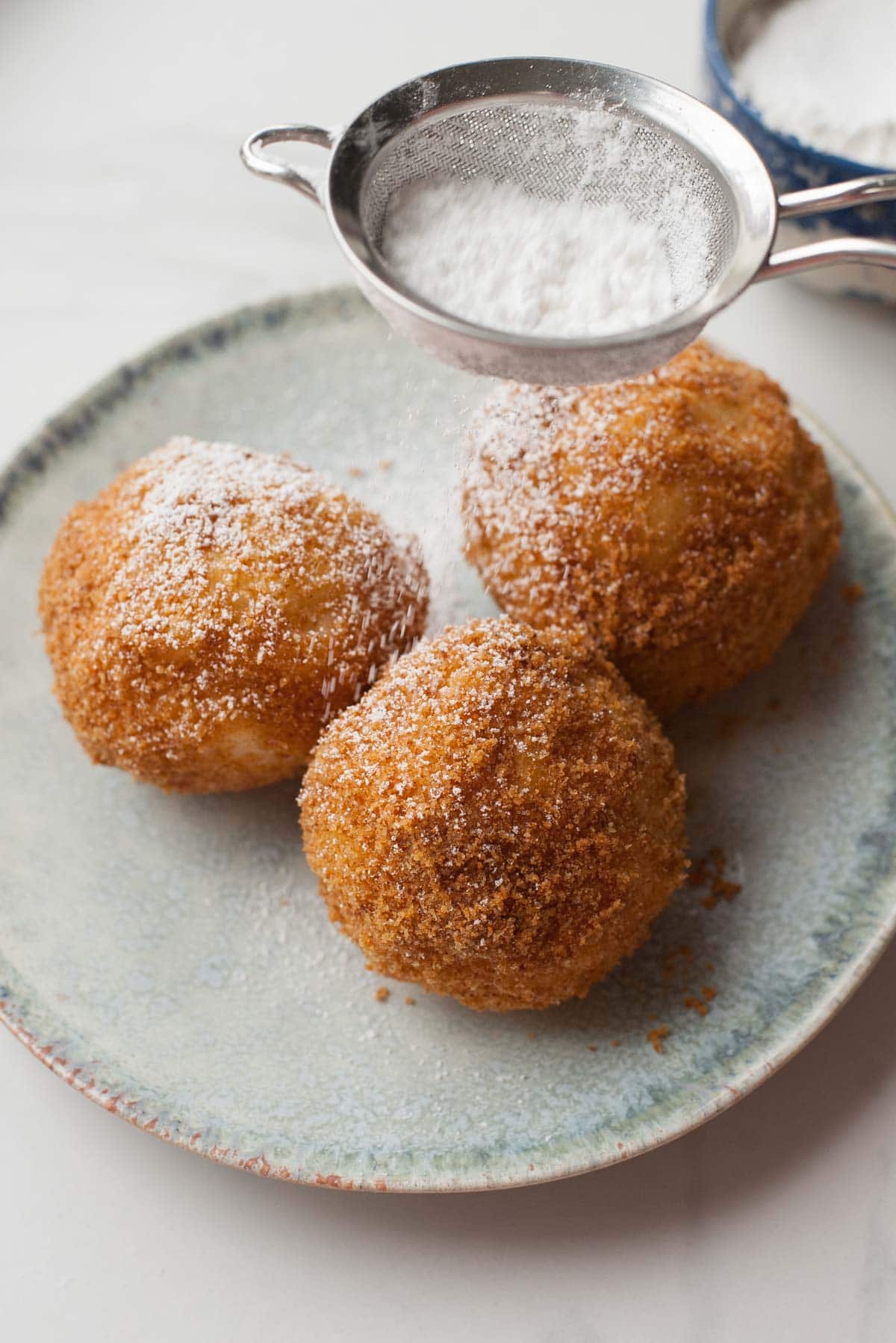 Apricot dumplings on a green plate are being sprinkled with powedered sugar.