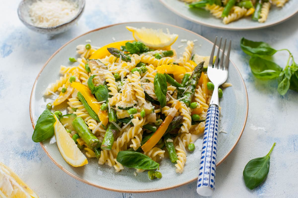 Pasta with vegetables and creamy sauce on a blue plate with a blue fork