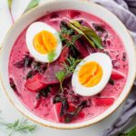 young beet soup in a white bowl, cooked eggs and dill in the soup