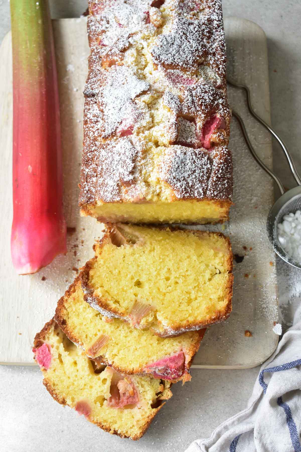 easy rhubarb cake on a white wooden board partially cut into slices