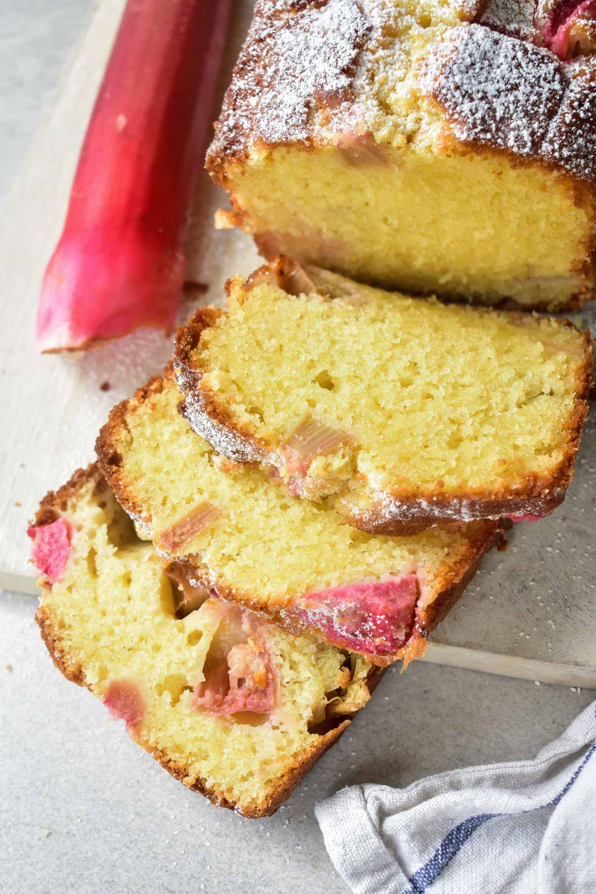 Rhubarb cake cut into slices on a white wooden board