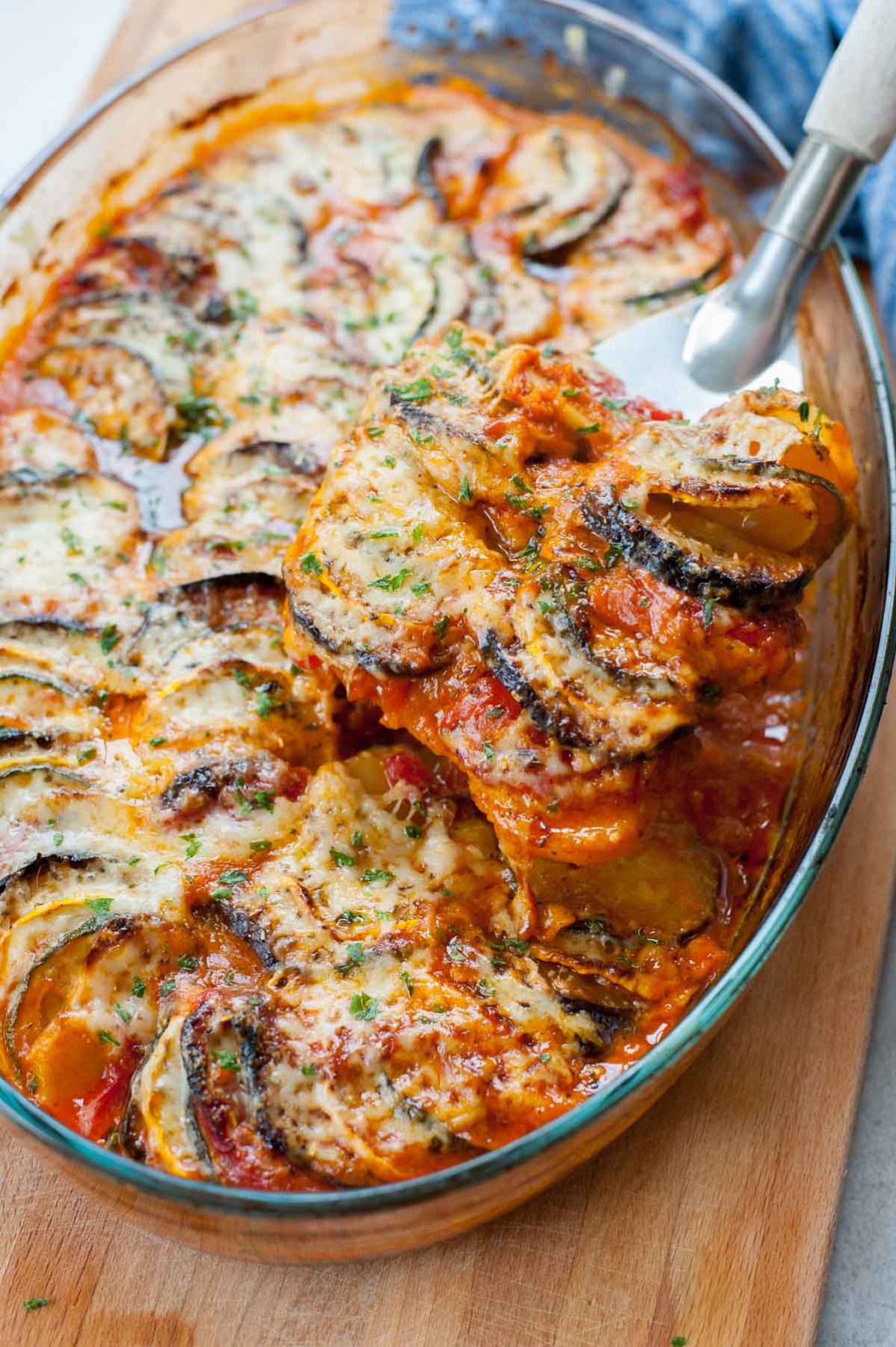 Baked ratatouille in a baking dish being scooped with a metal spatula.