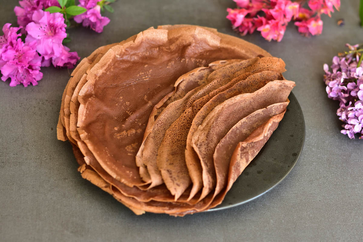 chocolate crepes on a black plate, flowers in the background