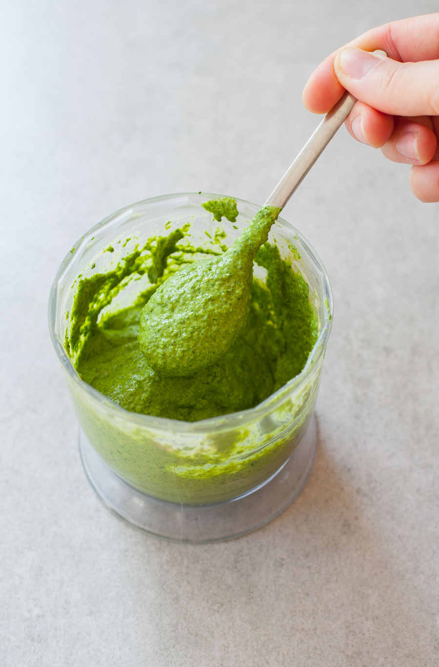 green tahini sauce in a food processor container spooned on a teaspoon
