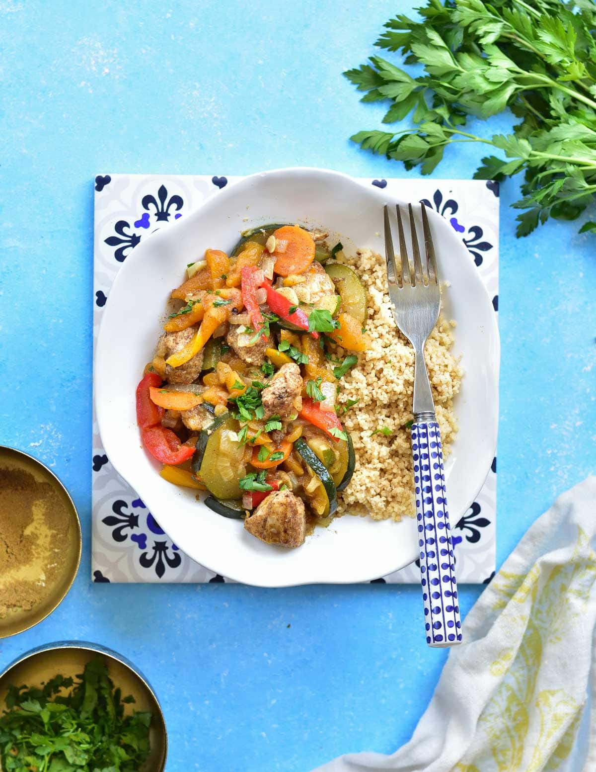 Moroccan chicken with dried apricots, vegetables and parsley couscous in a white plate on a blue background