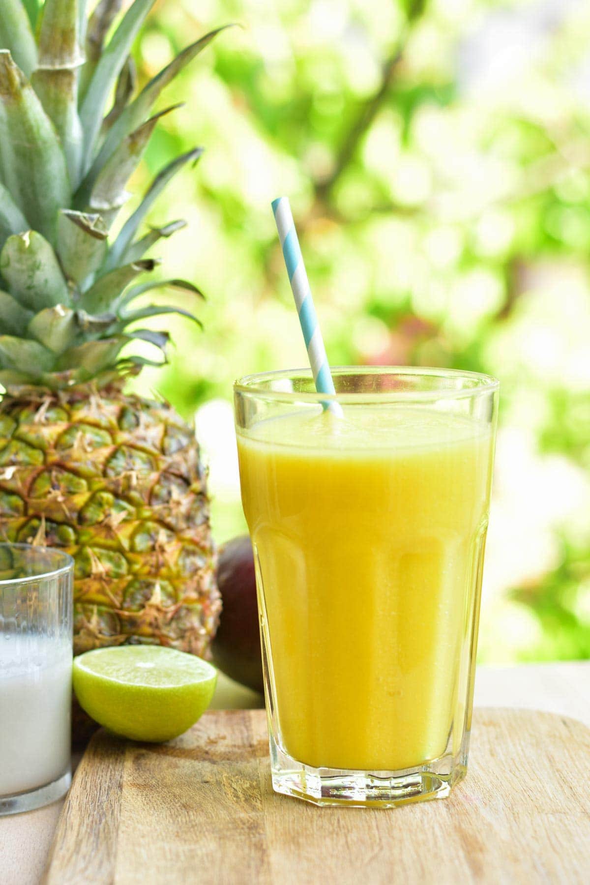 smoothie z ananasem, mango, mlekiem kokosowym i limonką w szklance na desce do krojenia