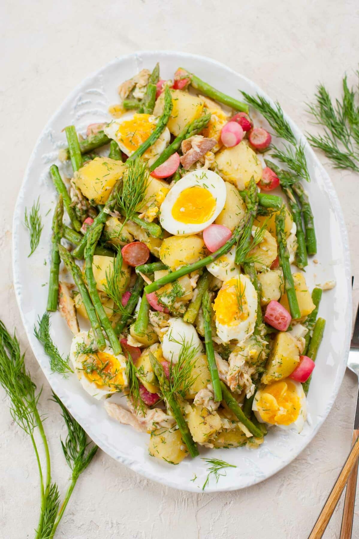 Potato and asparagus salad with eggs and smoked trout on a white plate