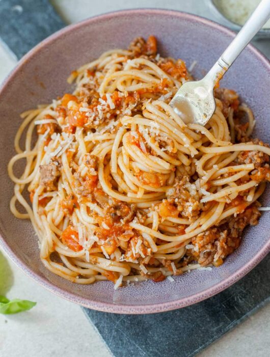 spaghetti with fresh tomato meat sauce on a fork in a violet bowl