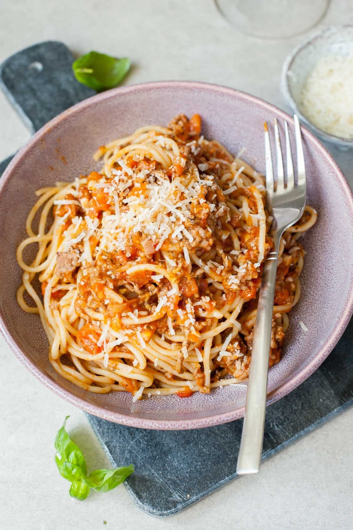 Szybkie spaghetti z mięsem i sosem ze świeżych pomidorów posypane parmezanem we fioletowej misce