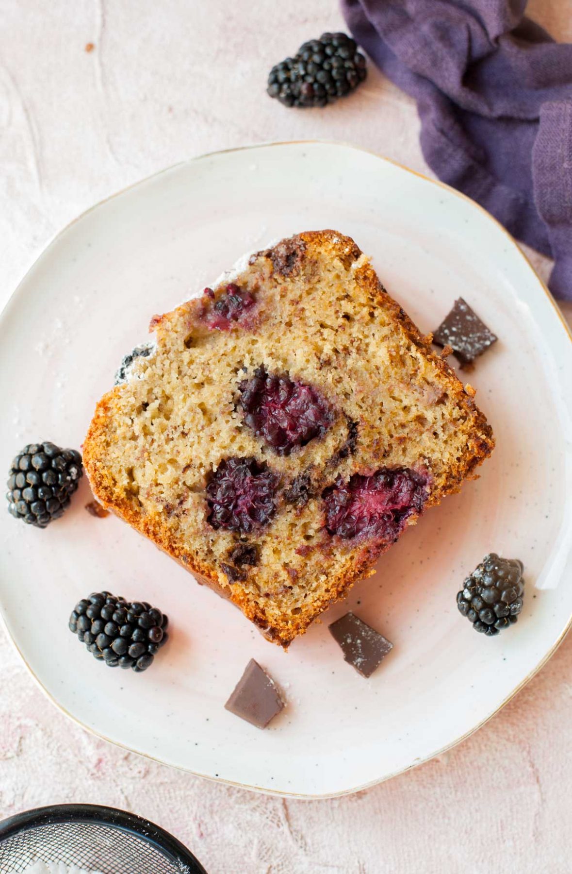 a slice of blackberry banana bread on a rosa plate, blackberries in the background