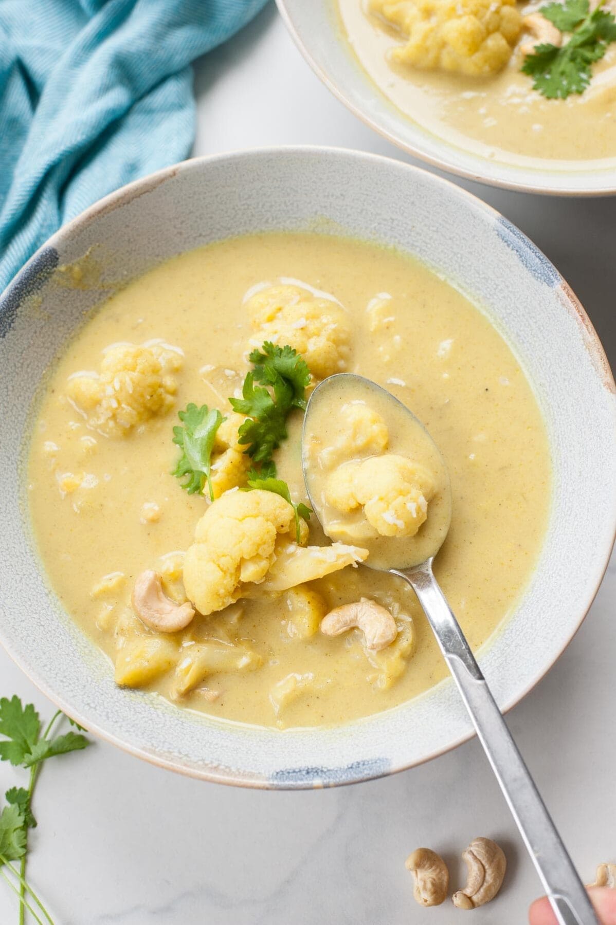 Curried cauliflower soup in a blue bowl is being scooped with a spoon