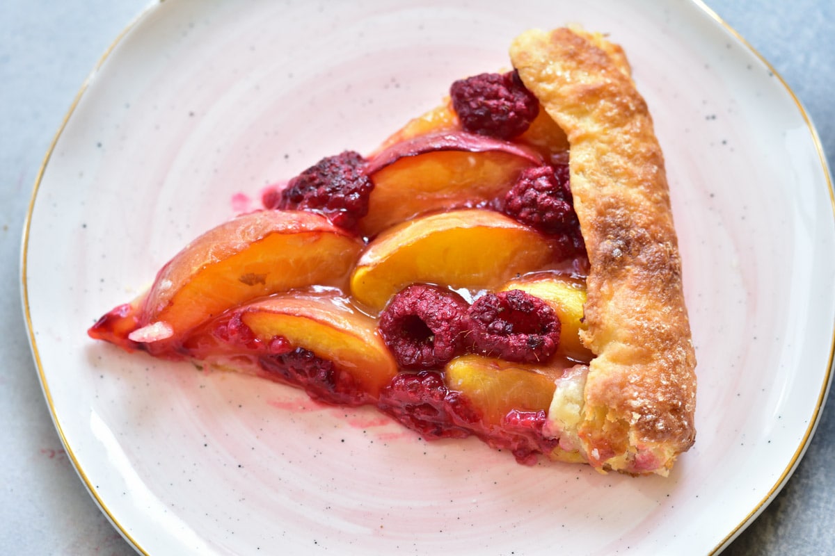 a piece of nectarine galette with raspberries on a rose plate