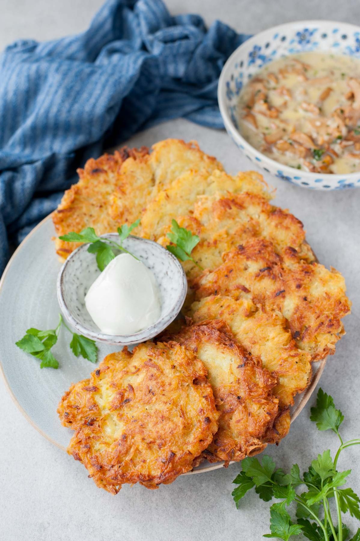 Potato pancakes on a blue plate, small bowl with sour cream, parsley and chanterelle sauce.