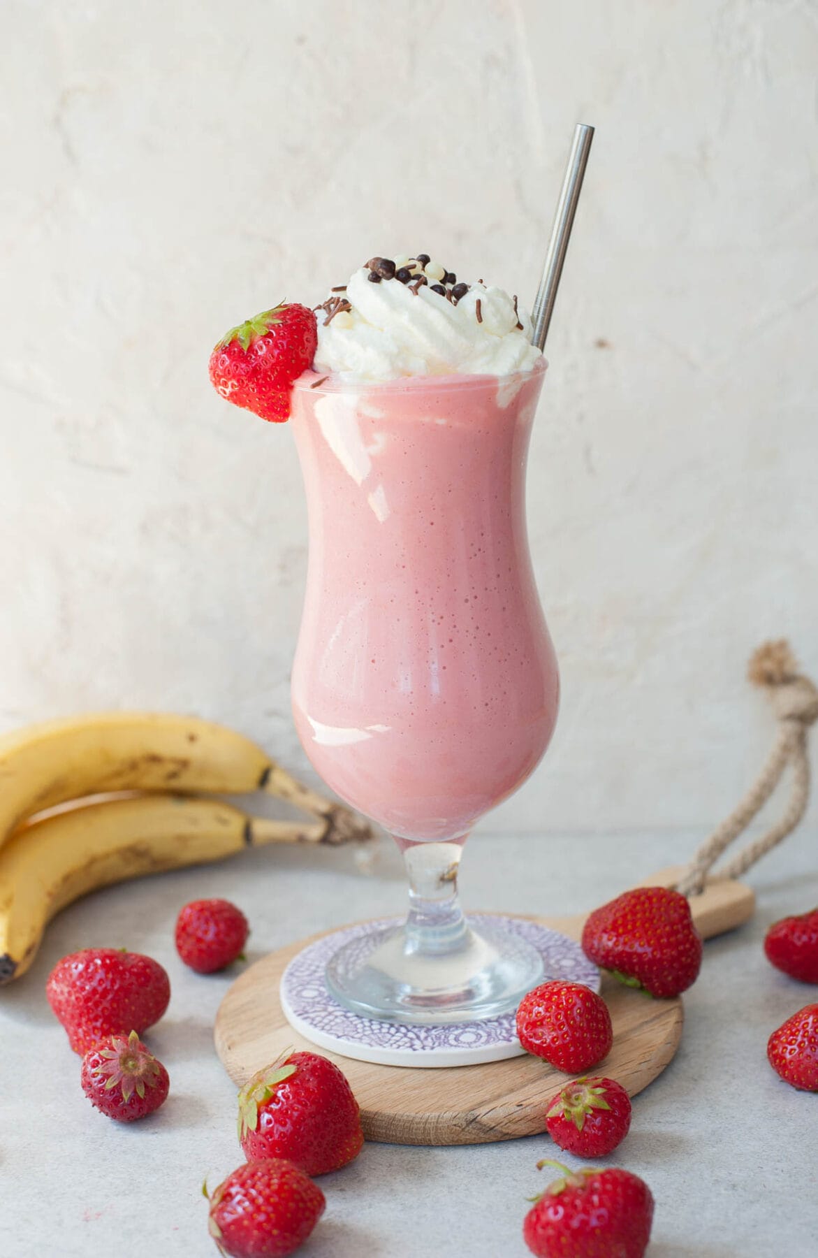 Strawberry banana milkshake in a highball glass with a straw and whipped cream