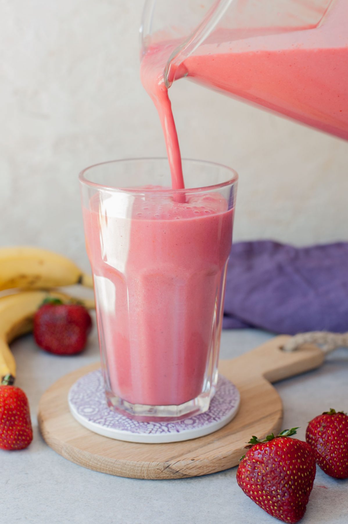 strawberry banana milkshake is being poured from a blender container to a high glass