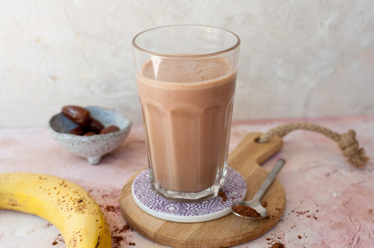 chocolate smoothie in a high glass, cocoa, bananas and dates in the background