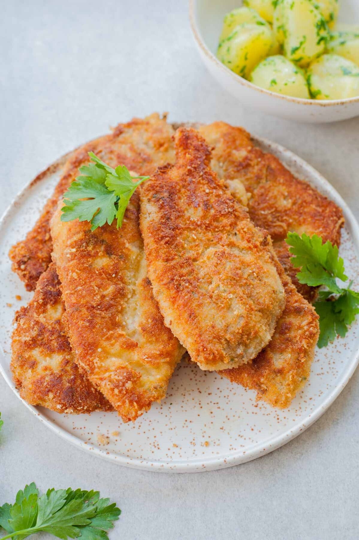 Breaded chicken cutlets on a white plate sprinkled with parsley.