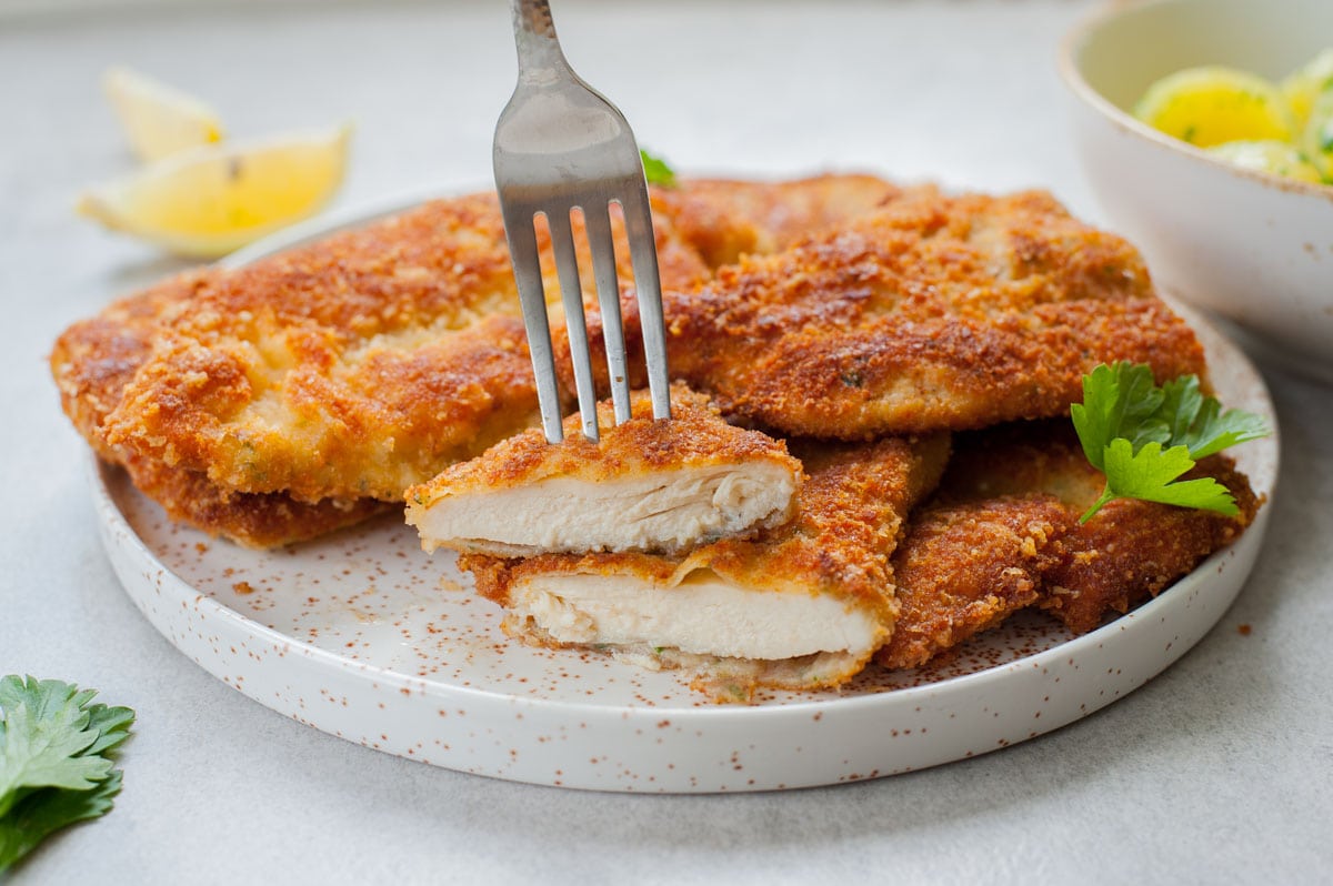 Breaded chicken cutlets cut in half and stuck on a fork.