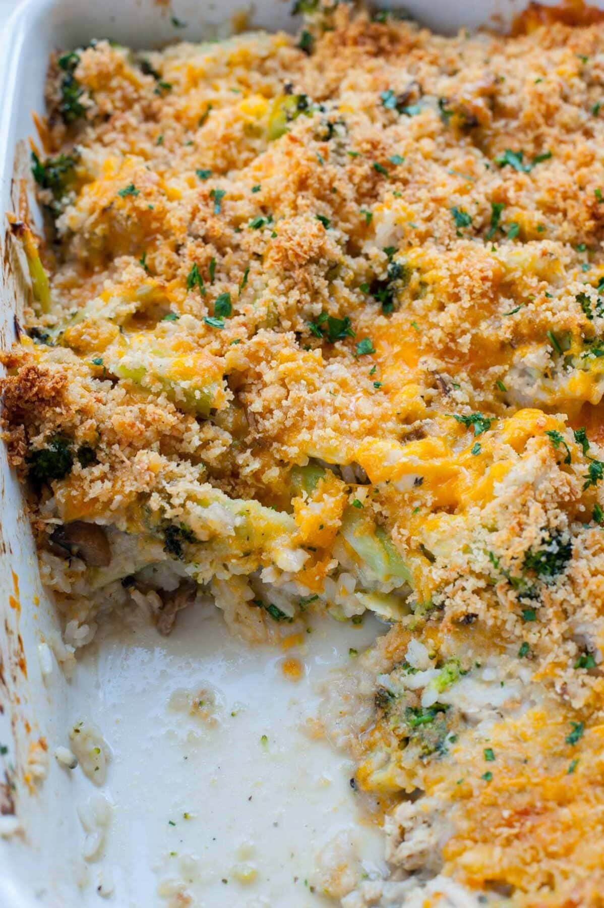 Chicken broccoli rice casserole in a white baking dish with one serving missing.