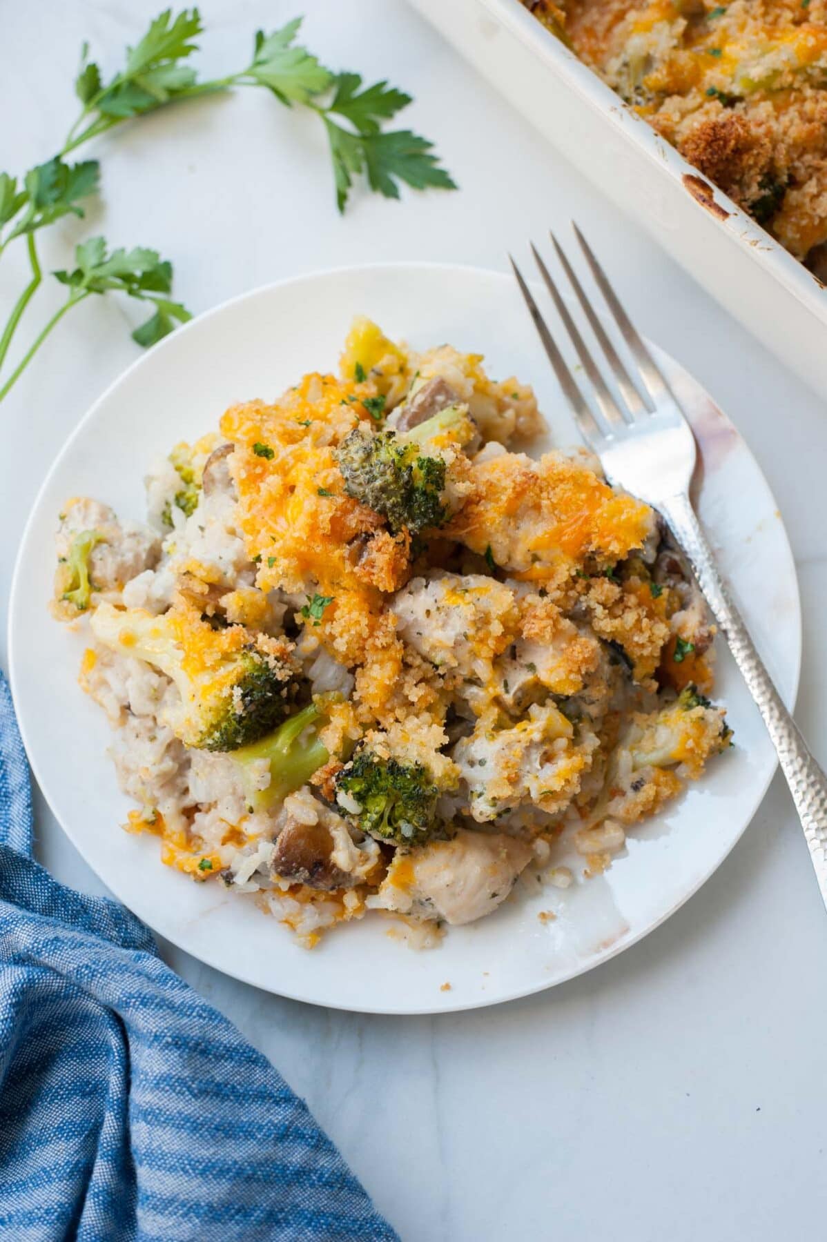 One serving of chicken broccoli rice casserole on a white plate, silver fork on the side.