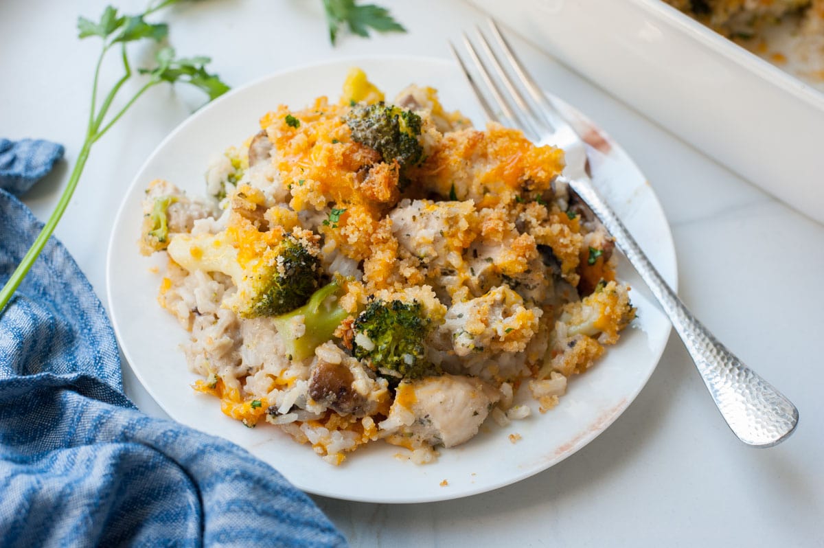 One serving of chicken broccoli rice casserole on a white plate, blue kitchen towel in the background.