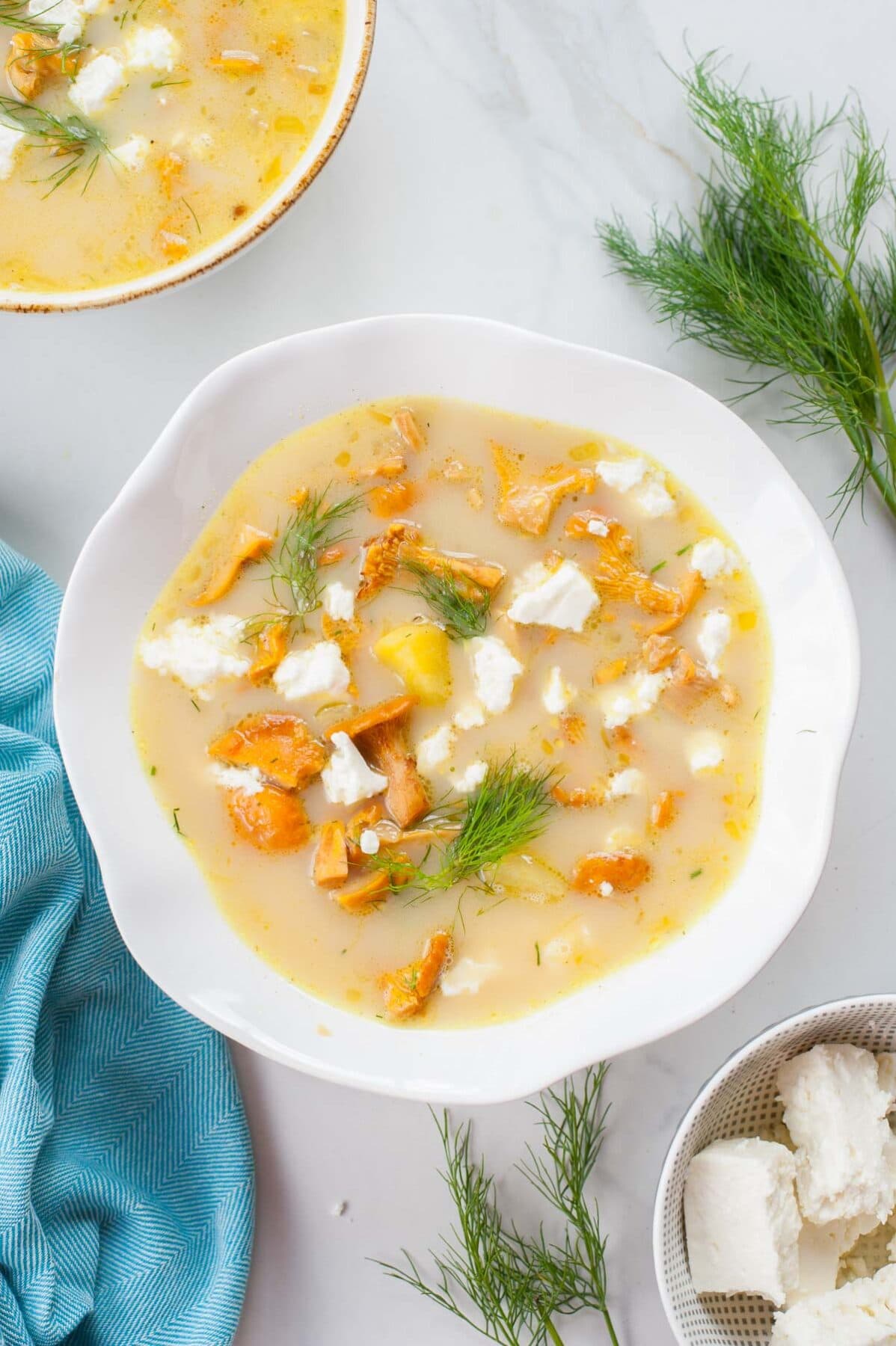 chanterelle soup in a white bowl, dill and a blue kitchen towel in the background