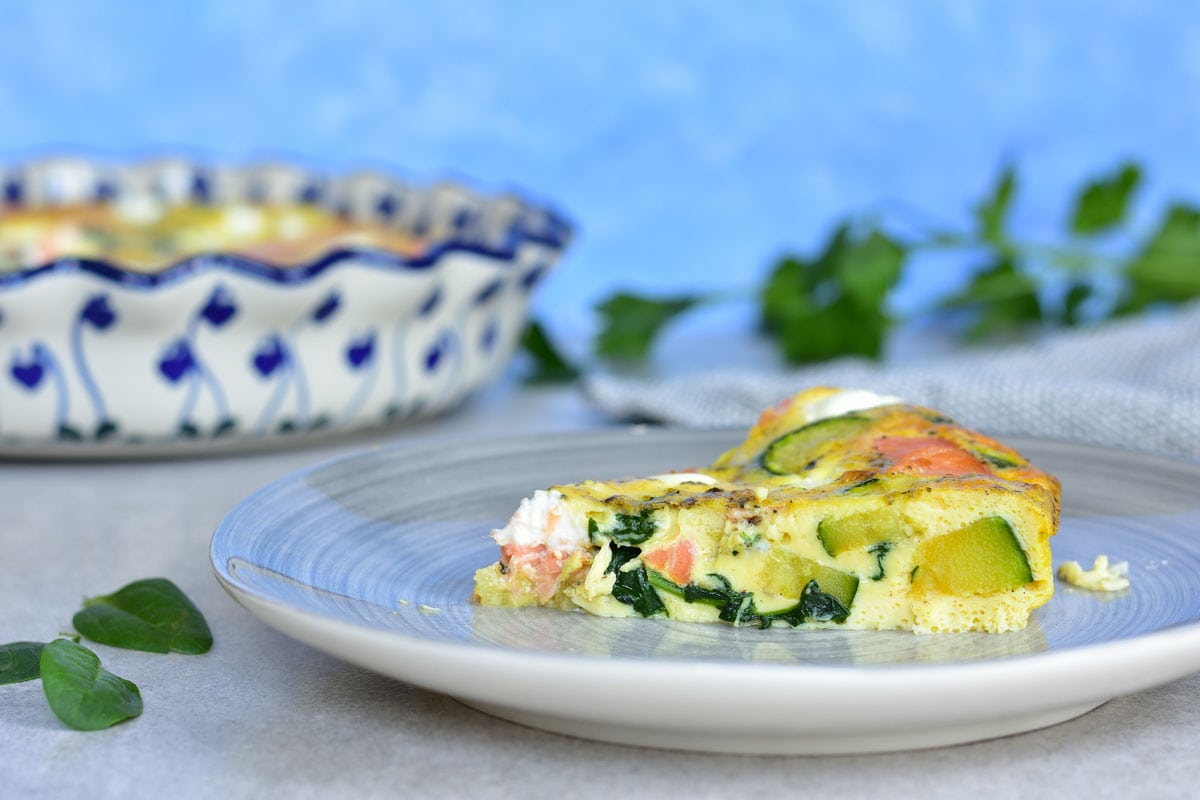 A piece of smoked salmon frittata on a grey plate, baking dish in the background.