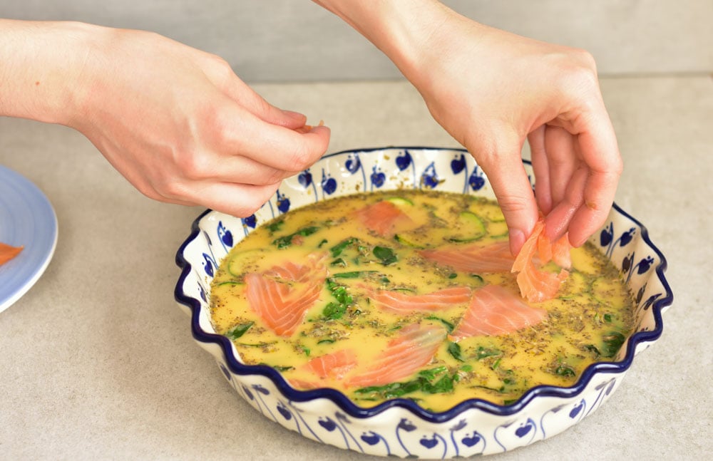 Smoked salmon is being added to the baking dish.