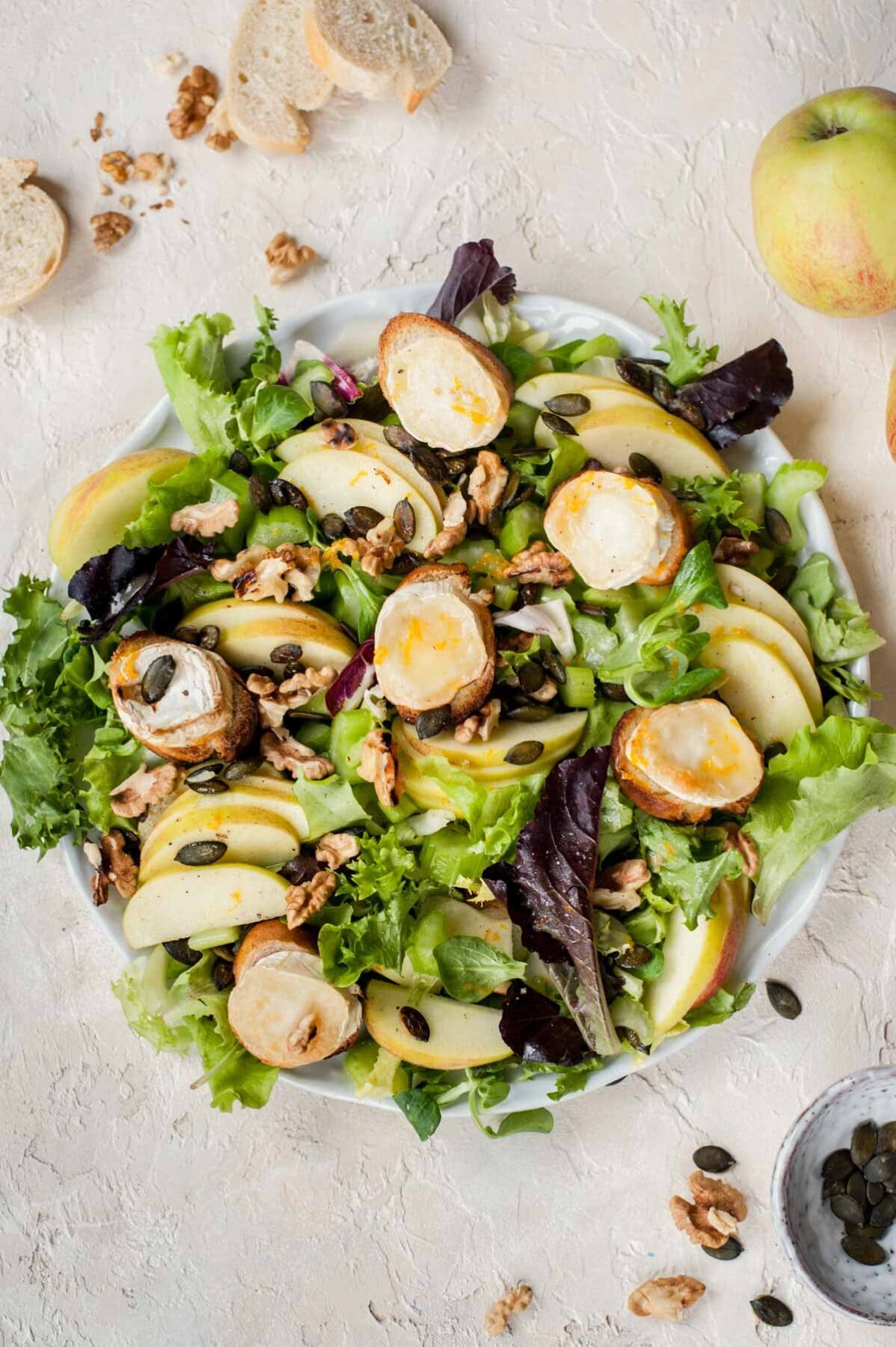 Overhead picture of apple celery salad with walnuts and goat cheese on a white plate.